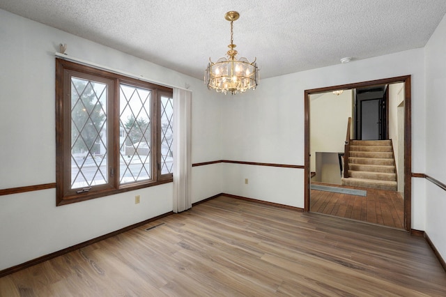 empty room featuring a textured ceiling, light wood finished floors, visible vents, and baseboards