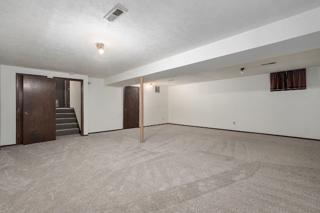 finished below grade area with stairs, visible vents, a textured ceiling, and light colored carpet