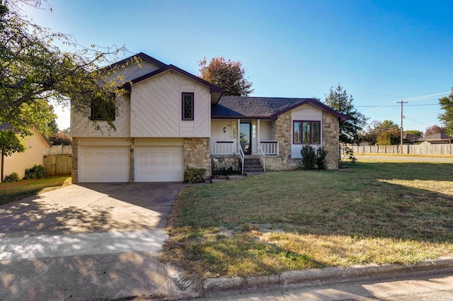 tri-level home with a garage, fence, concrete driveway, stone siding, and a front yard