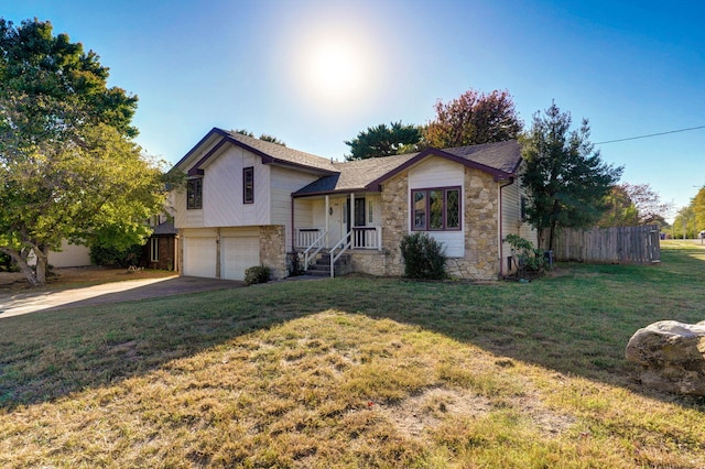 split level home featuring concrete driveway, an attached garage, a front yard, fence, and stone siding