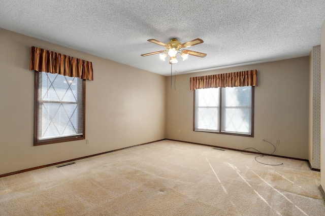 carpeted spare room with ceiling fan, a textured ceiling, visible vents, and baseboards