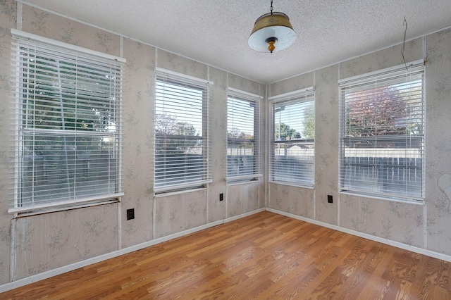 unfurnished room with a textured ceiling, baseboards, and wood finished floors