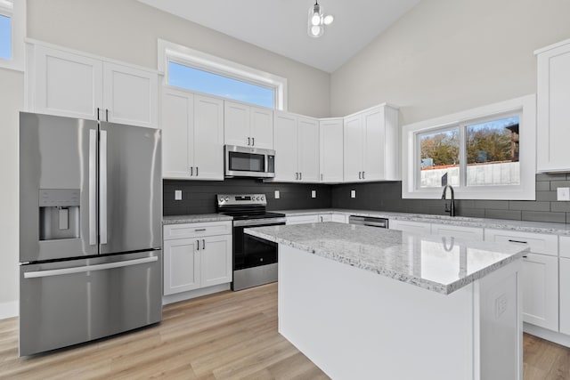 kitchen featuring lofted ceiling, light wood-style flooring, appliances with stainless steel finishes, a center island, and backsplash