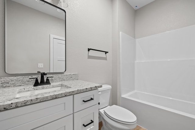 bathroom featuring a textured wall, vanity, toilet, and shower / bathtub combination