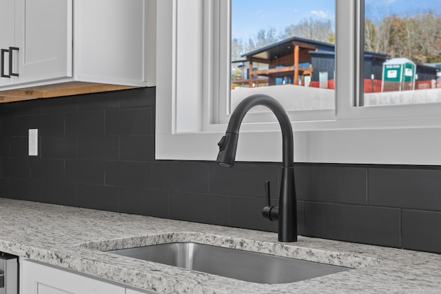 room details with light stone counters, tasteful backsplash, a sink, and white cabinetry