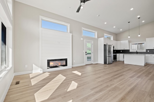 unfurnished living room featuring a high ceiling, a sink, visible vents, light wood finished floors, and a glass covered fireplace