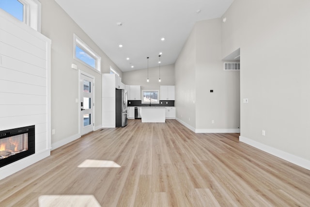 unfurnished living room with light wood finished floors, a fireplace, a towering ceiling, and visible vents