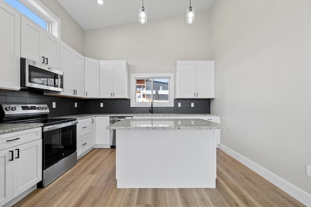 kitchen with a kitchen island, a towering ceiling, baseboards, appliances with stainless steel finishes, and backsplash