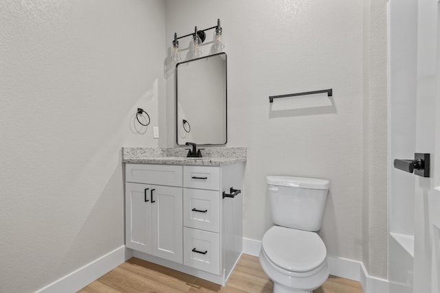 half bath featuring baseboards, vanity, toilet, and wood finished floors