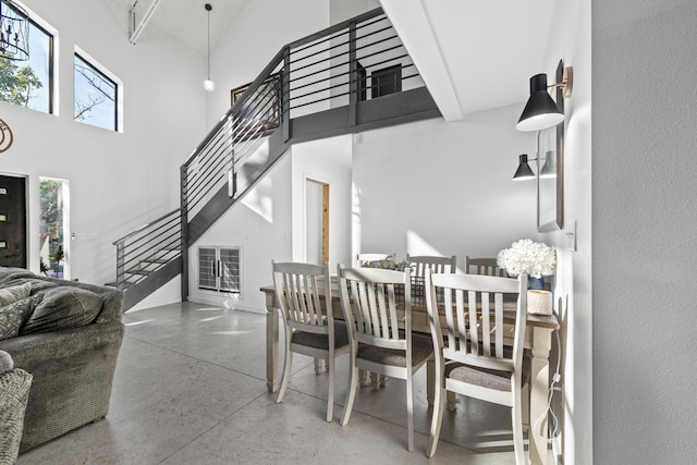 dining room with a high ceiling, stairway, and concrete flooring