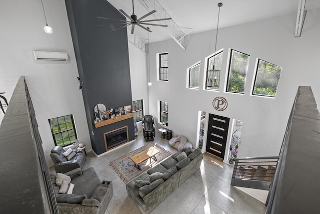 living room featuring ceiling fan, a high ceiling, a wall unit AC, and a glass covered fireplace