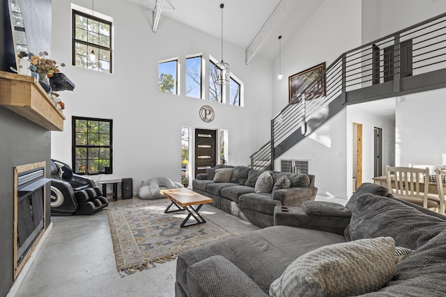 living area with a fireplace, finished concrete flooring, stairway, a high ceiling, and beamed ceiling