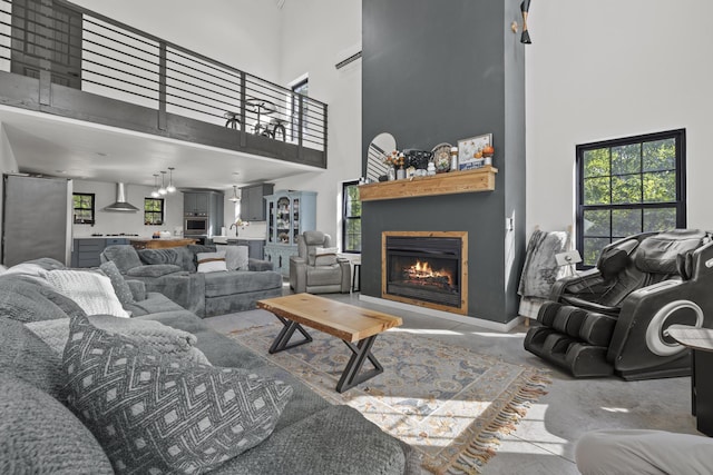 living room featuring a towering ceiling, a lit fireplace, and concrete floors