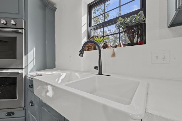 room details with stainless steel double oven, light countertops, a sink, and gray cabinetry