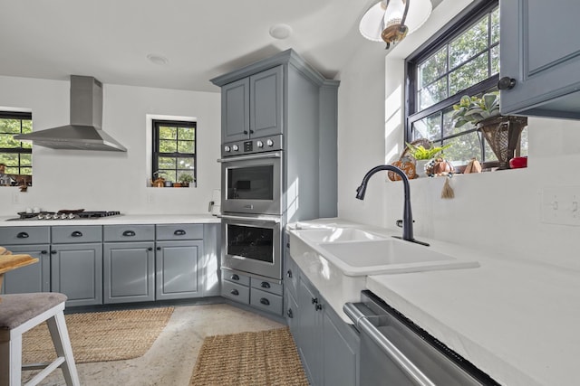 kitchen with stainless steel appliances, gray cabinets, a sink, and wall chimney range hood