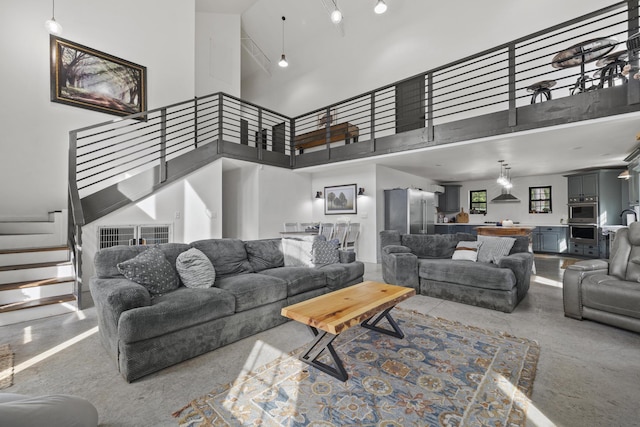 living area with finished concrete flooring, a towering ceiling, and stairs