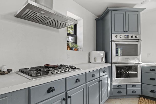 kitchen featuring wall chimney range hood, appliances with stainless steel finishes, light countertops, and gray cabinetry