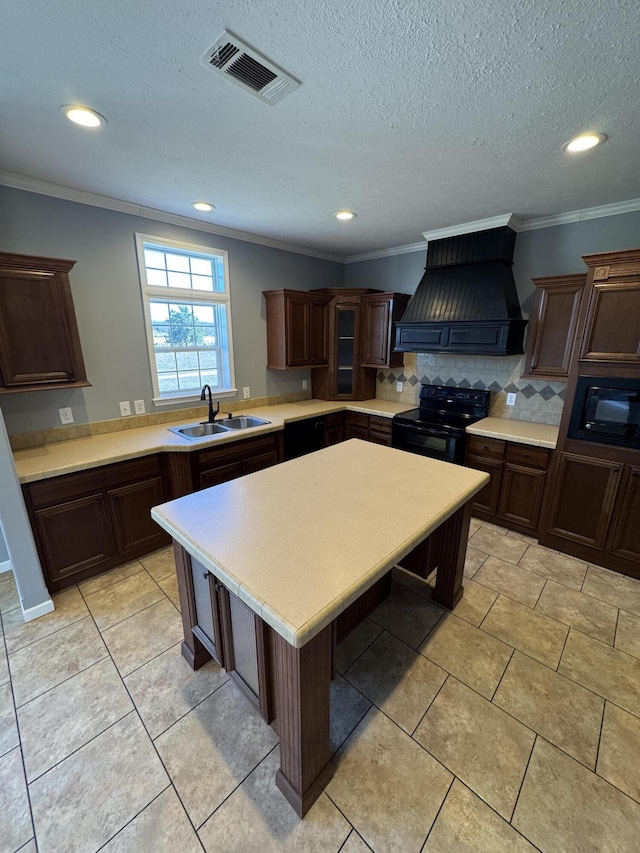 kitchen with visible vents, custom range hood, light countertops, black appliances, and a sink