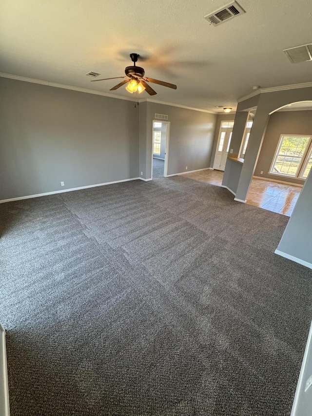 empty room featuring visible vents, arched walkways, crown molding, and carpet flooring