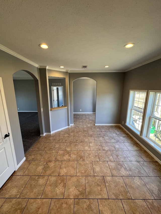 tiled spare room with arched walkways, ornamental molding, a textured ceiling, and baseboards