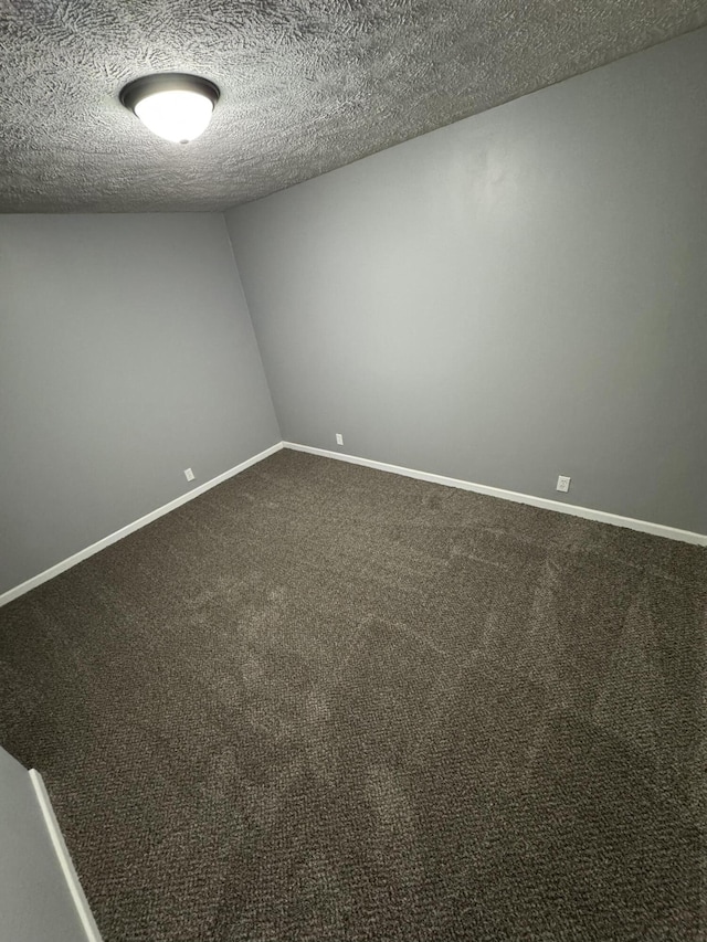 unfurnished room with lofted ceiling, baseboards, dark colored carpet, and a textured ceiling