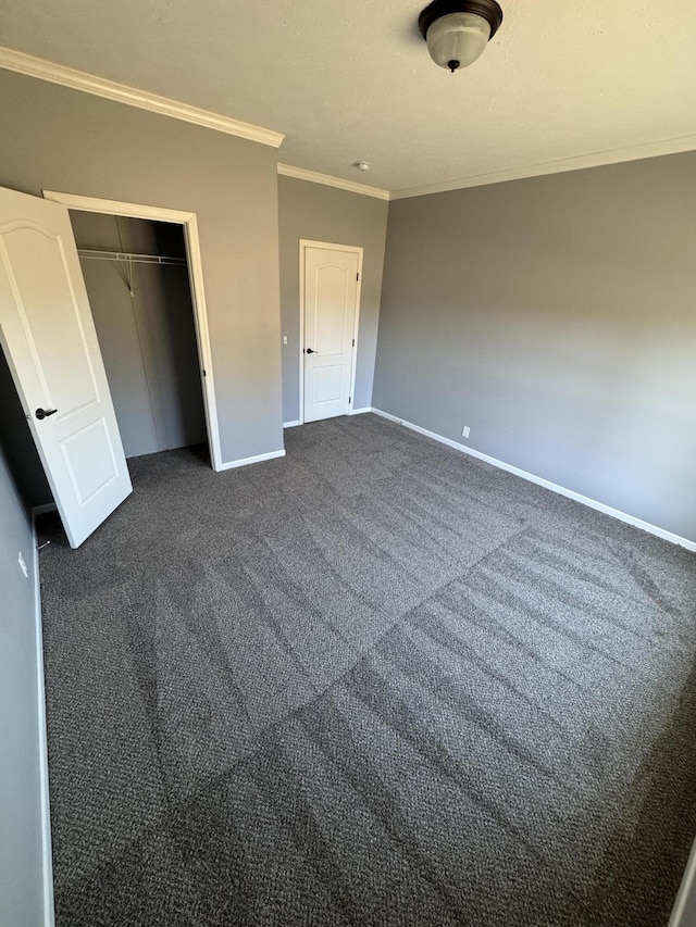 unfurnished bedroom with ornamental molding, a closet, dark carpet, and baseboards