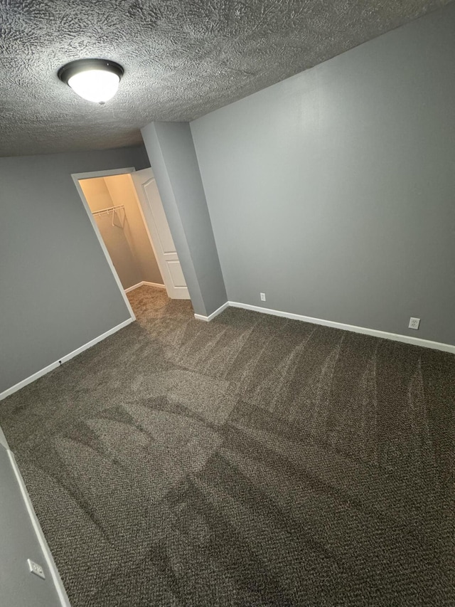 empty room with baseboards, dark carpet, and a textured ceiling