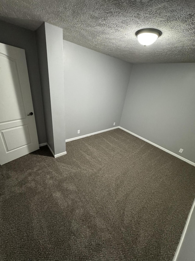 spare room featuring dark colored carpet, a textured ceiling, and baseboards