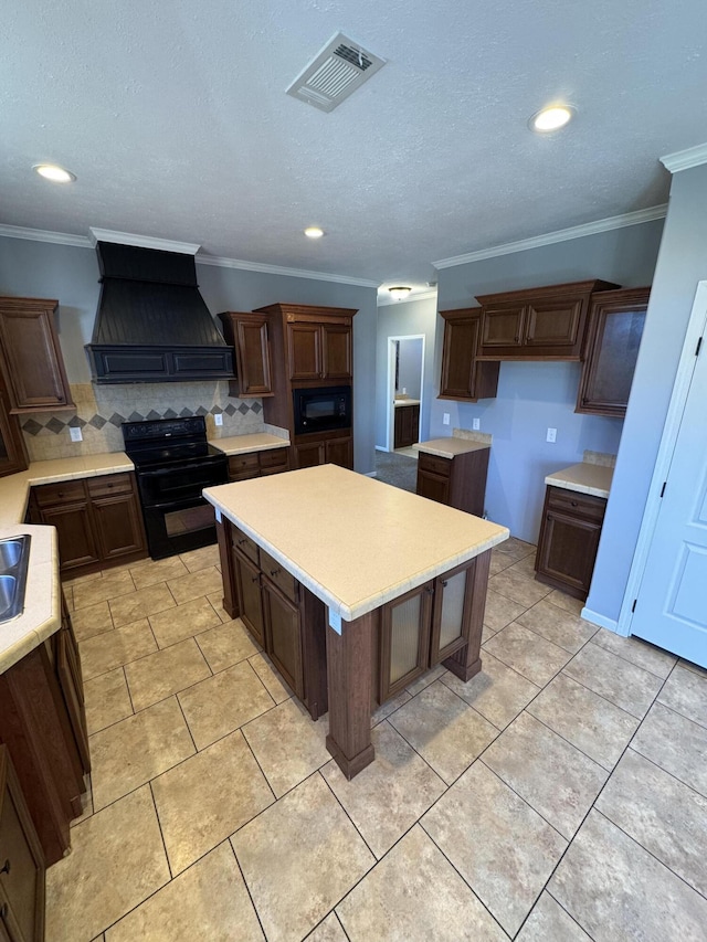 kitchen with tasteful backsplash, custom range hood, visible vents, a kitchen island, and black appliances