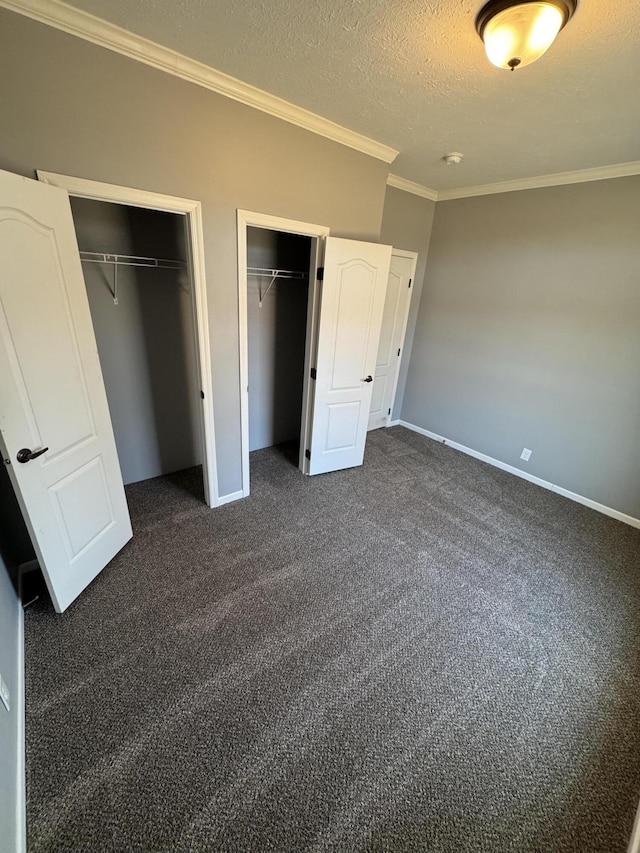 unfurnished bedroom with baseboards, ornamental molding, a textured ceiling, dark carpet, and multiple closets