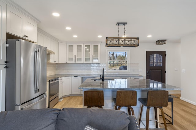 kitchen with appliances with stainless steel finishes, a breakfast bar area, light wood-type flooring, and white cabinetry