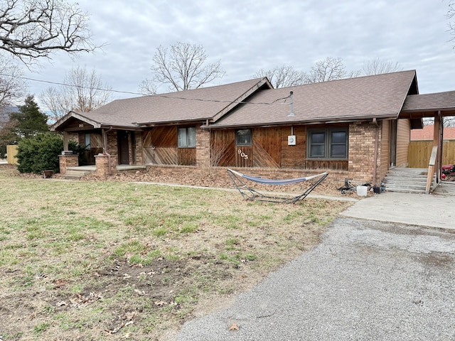 view of front facade featuring covered porch, a shingled roof, a front yard, and brick siding