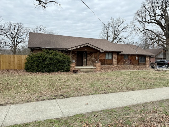 view of front of property featuring brick siding, a shingled roof, fence, and a front yard