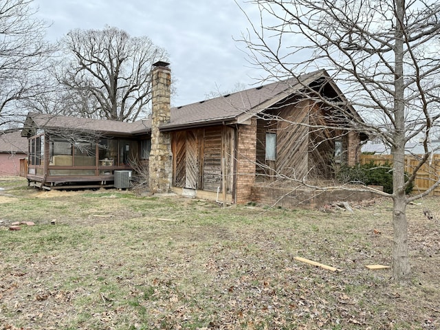 rear view of house featuring central AC unit, a shingled roof, a sunroom, a yard, and a chimney