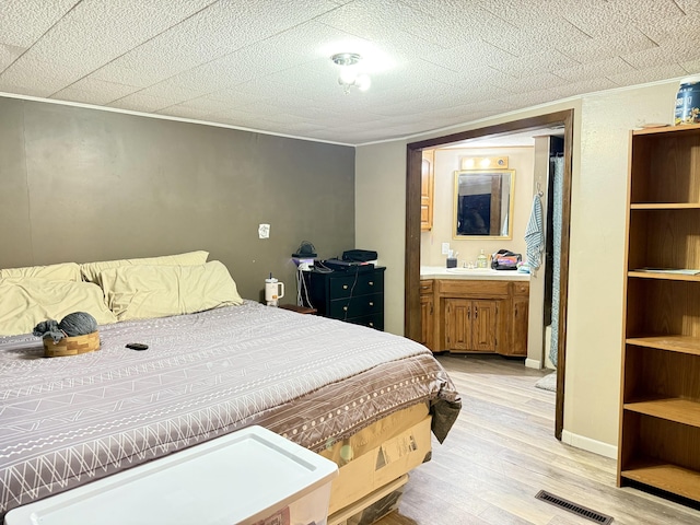 bedroom featuring ensuite bathroom, a textured ceiling, visible vents, baseboards, and light wood finished floors