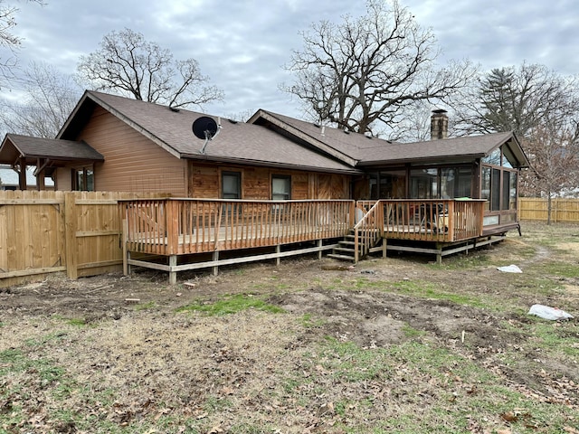 rear view of house featuring a deck, a chimney, fence, and a sunroom