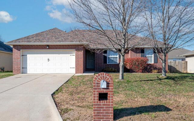 ranch-style home featuring an attached garage, driveway, brick siding, and a front yard