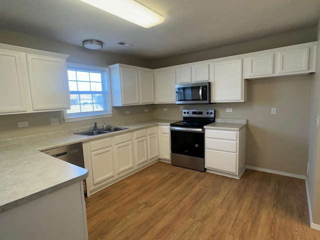 kitchen featuring light countertops, appliances with stainless steel finishes, white cabinetry, a sink, and light wood-type flooring