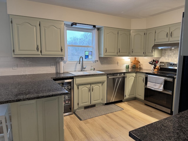 kitchen with light wood finished floors, beverage cooler, stainless steel appliances, under cabinet range hood, and a sink