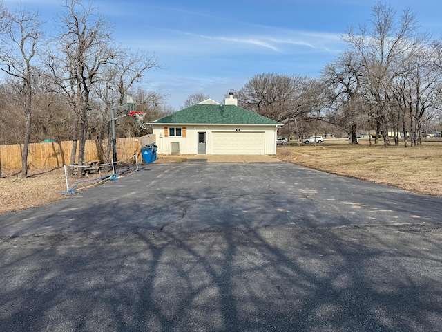 exterior space featuring a lawn, a chimney, aphalt driveway, an attached garage, and fence