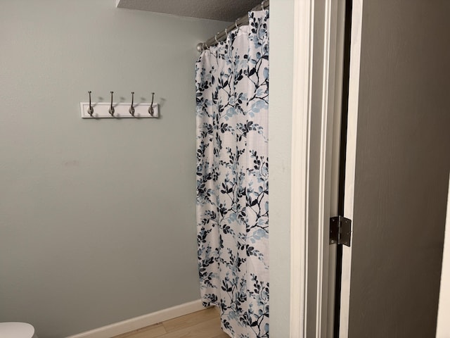 full bathroom featuring baseboards, wood finished floors, and a shower with shower curtain