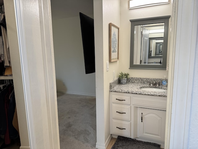 bathroom with a walk in closet, vanity, and baseboards