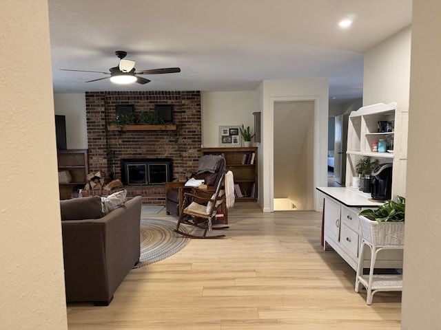 living area featuring a fireplace, light wood finished floors, and ceiling fan