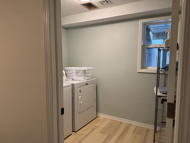 clothes washing area featuring washer and clothes dryer, light wood-style floors, a textured ceiling, laundry area, and baseboards