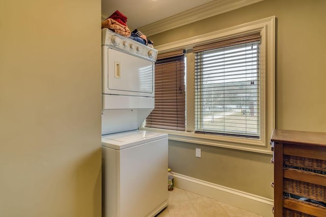 laundry room featuring stacked washer / drying machine, ornamental molding, light tile patterned flooring, laundry area, and baseboards