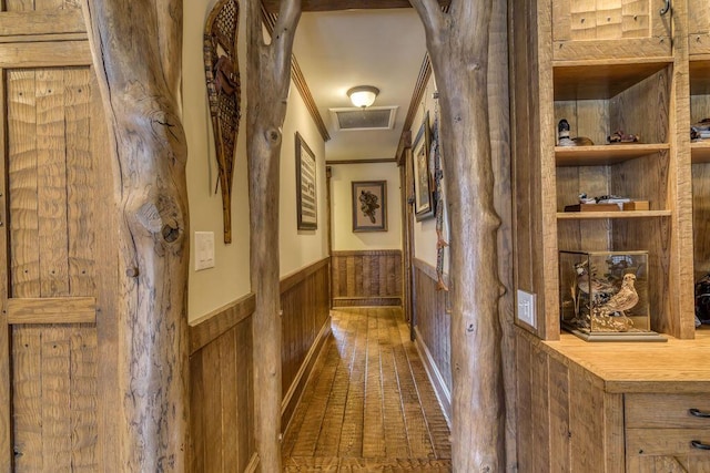 hall with arched walkways, visible vents, ornamental molding, wainscoting, and wood walls