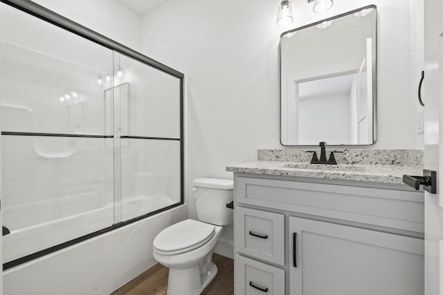 bathroom with toilet, bath / shower combo with glass door, wood finished floors, and vanity