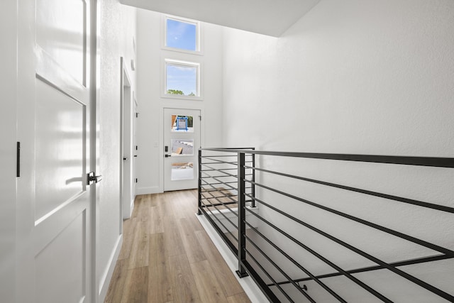 hallway featuring light wood-type flooring, baseboards, a high ceiling, and an upstairs landing