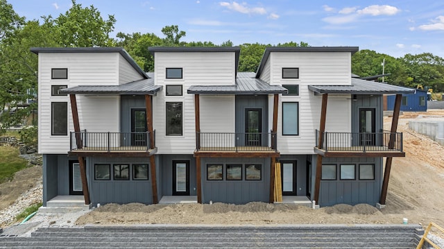 view of front facade with board and batten siding, metal roof, and a balcony