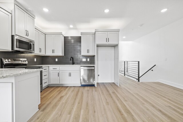 kitchen with light wood-style flooring, light stone counters, stainless steel appliances, backsplash, and recessed lighting